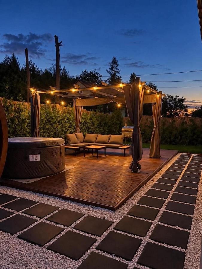 Kanapa pod oświetloną pergolą i grill na tarasie wieczorem